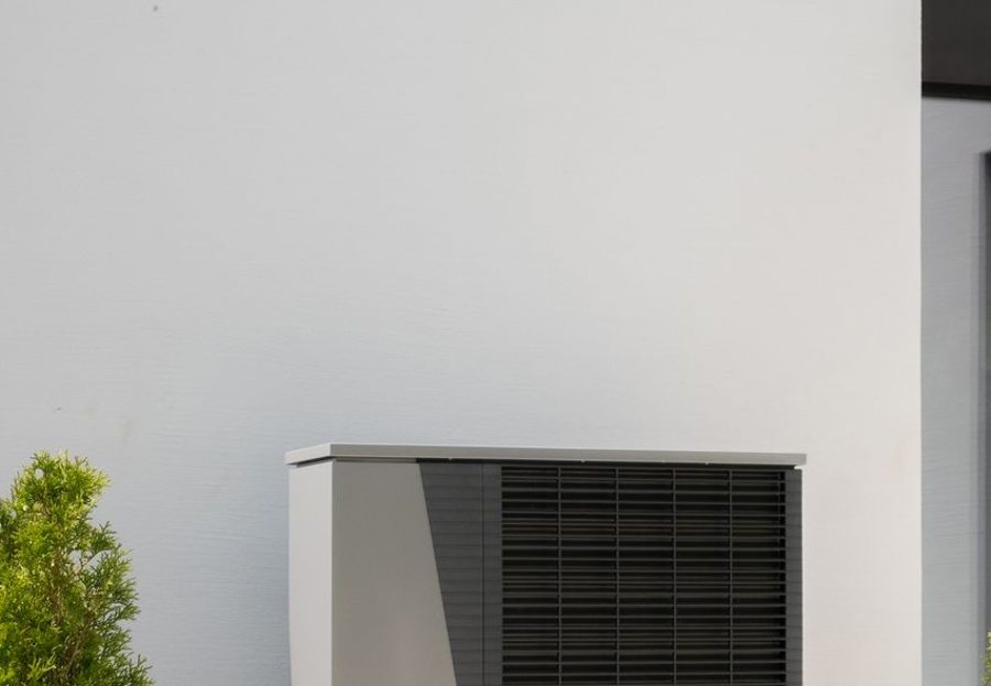 Air source heat pump outdoor unit installed against a house wall